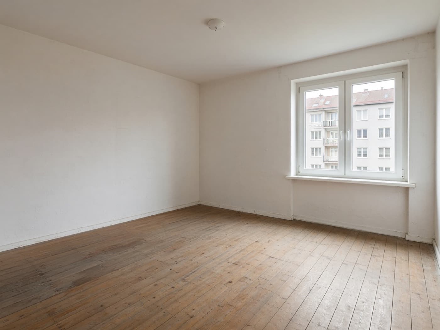 Leere Wohnung mit Dielenboden und Fenster nach der Entrümpelung.